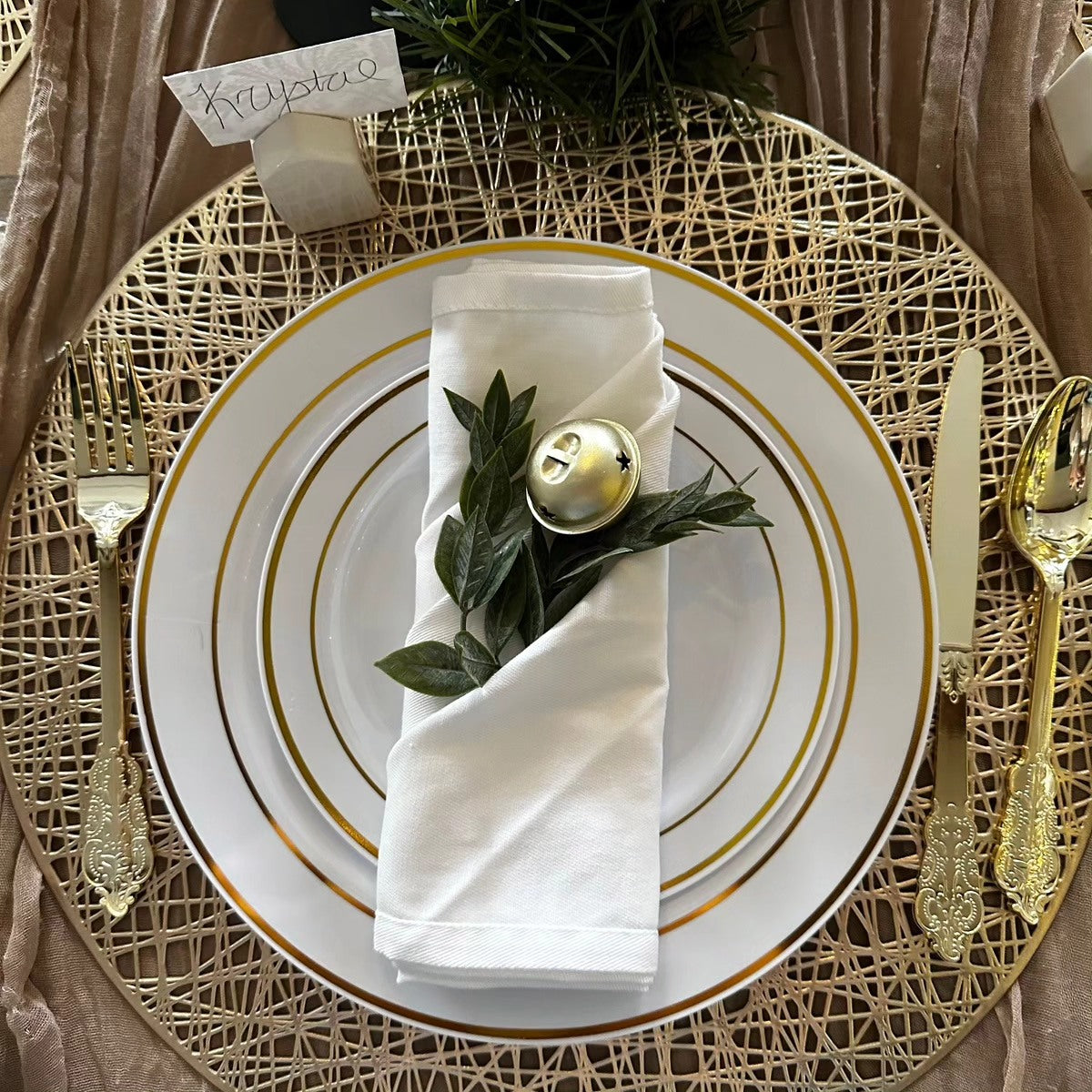 Elegant place setting featuring gold and white disposable Christmas plates with polished silverware.