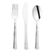 A set of Kaya Collection's Shiny Metallic Silver Hammered Plastic Cutlery, featuring a fork, knife, and spoon arranged in a row. Each utensil boasts a textured, hammered handle that adds a decorative flair to the practical design. The surfaces are shiny and reflective.