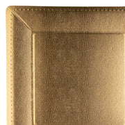 A close-up of the corner of a gold-colored, rectangular plate reveals its textured surface with a subtle pattern. The slightly raised edges feature fine, beaded detailing that resemble stitching. This sophisticated design brings to mind elegant paper plates for both stylish dining and decorative purposes, perfectly captured by the Gold Square Edge Beaded Disposable Paper Charger Plates (13") from Kaya Collection.