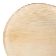 Close-up photograph of a smooth, round, light brown *Round Palm Leaf Eco Friendly Disposable Dinner Plate (10")* by *Kaya Collection*, with a subtle visible grain pattern. The top-right edge of the plate is slightly out of frame. The surface has a natural, unfinished appearance reminiscent of eco-friendly disposable dinner plates.