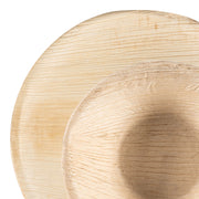 A close-up of a wooden soup bowl placed inside a larger wooden plate, both showcasing the natural, textured wood grain pattern and a light finish. The image highlights the simplicity and rustic elegance of the Round Palm Leaf Eco Friendly Disposable Dinnerware Value Set by Kaya Collection.