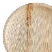 A close-up view of the Round Palm Leaf Eco Friendly Disposable Buffet Plates (9") showcases an eco-conscious and stylish option for your dining needs. These 9-inch plates are crafted from natural, textured palm leaves and exhibit a blend of light beige and brown tones with visible grain patterns that underscore their organic origins. Ideal for compostable buffet settings.