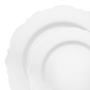 Two overlapping plates from the White with Silver Rim Round Blossom Disposable Plastic Dinnerware Value Set, featuring scalloped edges and a gentle wave-like pattern, are positioned against a plain white background. The subtle decorative design of the edges adds an elegant touch, making them perfect for party use.