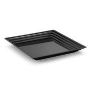 A 16" x 16" black square serving tray from the Kaya Collection, featuring a grooved rim and a smooth, flat base, is displayed. This BPA-free plastic tray showcases a modern design and is slightly elevated above the surface it rests on. Set against a white, uncluttered background, the details of the tray are prominently highlighted.