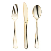 A close-up image of a polished Gold Classic Cutlery Plastic Silverware Set by Kaya Collection set against a white background. The set includes a fork with four tines, a serrated knife, and a spoon, all with sleek, modern designs and slightly rounded handles.