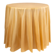 A round table adorned with a smooth, draped Gold Round Disposable Plastic Tablecloth (84") extending to the floor. The fabric has a slight sheen and appears slightly translucent, providing a rich, elegant look reminiscent of golden-yellow hues. The plain white background emphasizes the tablecloth as the focal point.