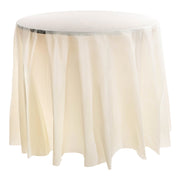 An 84" Ivory Round Disposable Plastic Tablecloth drapes elegantly over a round table, reaching down to the floor. The tablecloth features minimal folds and presents a soft, airy appearance. Set against a plain white background, the focus is entirely on the table and its stylish covering.