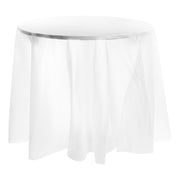 A White Round Disposable Plastic Tablecloth (84") drapes elegantly over the round table, reaching almost to the floor. The tablecloth's slightly translucent quality creates a soft and airy appearance, complementing the smooth, flat surface of the table.