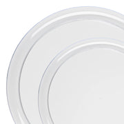 Image of two Kaya Collection Clear Flat Round Disposable Plastic Dinnerware Value Set plates with subtle, slightly overlapping rims. The edges of the plates have a thin, decorative line providing a simple yet elegant design. The background is white, highlighting the transparency and sophistication of these elegant disposable plates.