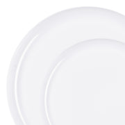 Two plain white, round high-quality lightweight plates from the White Flat Round Disposable Plastic Dinnerware Value Set are shown stacked slightly offset from each other on a white background. The larger plate is on the bottom, and the smaller one is on top, partially covering it. These disposable plastic dinnerware pieces offer a clean, minimalist design perfect for convenient party meal solutions.