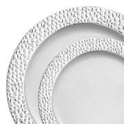 Two Kaya Collection White with Silver Hammered Rim Plastic Dinnerware plates are stacked on top of each other. The larger plate, serving as the base, partially supports the smaller top plate. Each plate boasts an intricately textured, hammered silver rim around their edges, while the center remains smooth and plain.