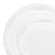 A close-up of two overlapping elegant plates from the Kaya Collection’s Clear with Silver Vintage Rim Round Disposable Plastic Dinnerware Value Set, showcasing an intricate, embossed floral pattern along the edges. The scalloped rim design adds an elegant touch to their appearance. The white background emphasizes the detailed craftsmanship of this value set.