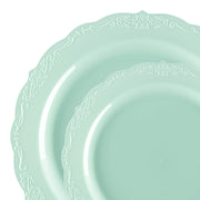 Two plates from the Turquoise Vintage Round Disposable Plastic Dinnerware Value Set feature an elegant light teal color with intricate floral and vine patterns along their scalloped edges. The plates are stacked partially within each other, showcasing the beautiful design on their edges. The background is white and seamless.