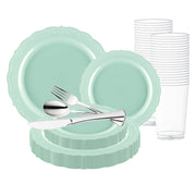 A collection of turquoise plastic plates in various sizes from the Turquoise Vintage Round Disposable Plastic Wedding Value Set is displayed, along with silver plastic cutlery including a spoon, fork, and knife. Stacked clear plastic cups are positioned on the right-hand side of the image. This elegant setting offers service for 20.