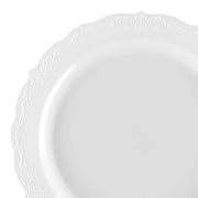 An image of a White Vintage Round Disposable Plastic Dinner Plate by Kaya Collection, featuring elegant, intricate decorative patterns along the rim. This 10" plate boasts a glossy finish and a slightly wavy edge, exuding a classic and sophisticated appearance. These wedding party plates are simple yet stylish, perfect for any special occasion.