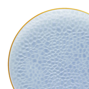 A close-up of an elegant round plate from the Kaya Collection, featuring a pale blue, hammered glass surface pattern. The plate is accented with a delicate gold-colored rim around its edge. The background is plain white.