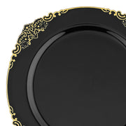 A close-up of a Black with Gold Fancy Round Disposable Plastic Salad Plate (7.5"), featuring intricate floral and scroll patterns, showcased against a white background. This elegant plate exudes sophistication and luxury while maintaining the convenience of disposable plastic plates.