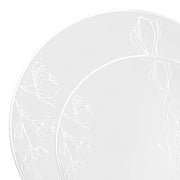 Two plates from the White with Silver Antique Floral Round Disposable Plastic Dinnerware Value Set feature a subtle, almost silver antique floral motif etched around the edges. The design showcases delicate flowers and leaves in a light, elegant pattern. These romantic dinnerware plates are positioned slightly overlapping each other.