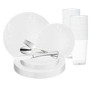 The White with Silver Antique Floral Round Disposable Plastic Wedding Value Set features a set of white disposable plates adorned with floral patterns, accompanied by silver disposable cutlery including a knife, spoon, and fork, neatly arranged in a stack. In the background, transparent plastic cups are stacked in two rows. This elegant disposable plastic dinnerware provides service for 20.