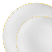 Two white plates with gold rims from the Kaya Collection's White with Gold Rim Organic Round Disposable Plastic Dinnerware Value Set are pictured, one slightly overlapping the other. The larger plate is partially visible in the background, while the smaller plate is in the foreground. This elegant dinnerware design is simple and refined, emphasizing clean lines and color contrast.