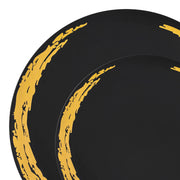 Two pieces from the Black with Gold Moonlight Round Disposable Plastic Dinnerware Value Set, featuring black plates adorned with artistic golden brushstroke designs along the edges, arranged in a partially overlapping manner. Each plate showcases a streaked, abstract pattern, lending a contemporary and sophisticated touch to this elegant dinnerware set.