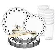 A collection from the White with Black Dots Round Blossom Disposable Plastic Wedding Value Set featuring white plates with a scalloped edge and black polka dots, complemented by stacks of clear plastic cups and a set of gold-colored cutlery, including knives, forks, and spoons.