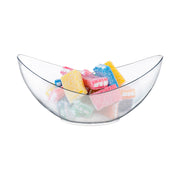 A transparent glass bowl filled with vibrant sugar-coated gummy candies, shaped like small rectangular blocks in yellow, pink, blue, and green. Nearby, 4 oz. Clear Big Disposable Plastic Concave Cups are scattered around. The bowl is placed against a plain white background.